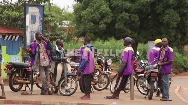 Мужчины - африканцы в сиреневой униформе стоят у мотоциклов на обочине дороги. Один из них...