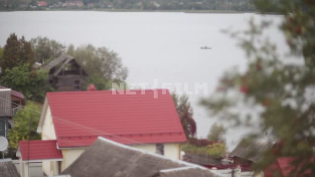 Вид на озеро через красные черепичные крыши домов, на озере небольшое судно Вид на озеро через...