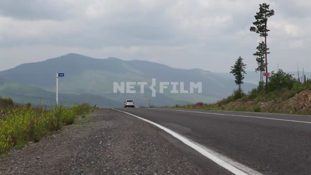 On the road between the mountains low riding cars on the roadside - flowering plants,...
