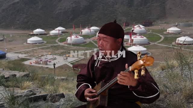 Тувинский музыкант играет на национальном музыкальном инструменте на фоне юртового лагеря....