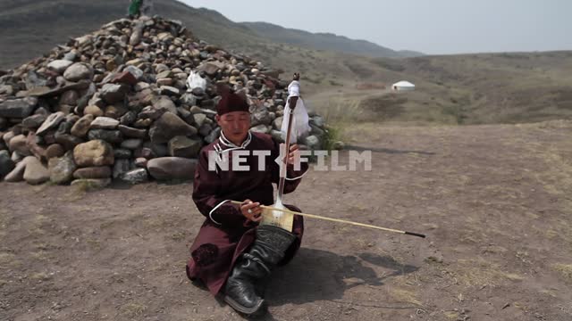 Tuvan musician playing on the national musical instrument ISIS amid mountains and picturesque piles...