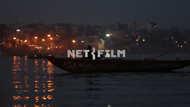 Люди сидят в лодке на реке в вечернем сумраке на фоне огней с берега Лодка, люди, огни, река,...