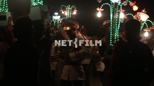 по ночной улице индийского города шествие индийских мужчин с фонарями в виде цветов и индийских...