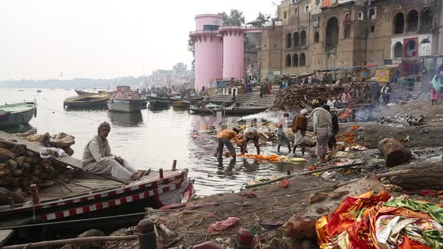 Indian men on the riverbank near the temple, on the steps of the temple, sitting in boats in the...