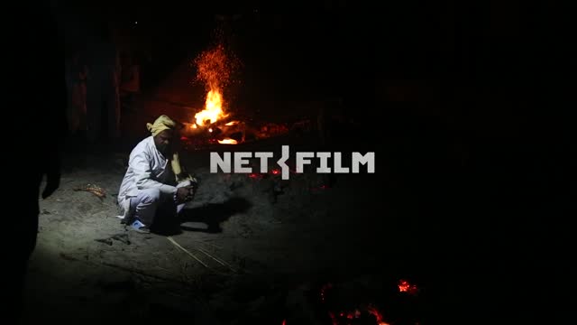 Indian sorcerer in the night standing there in front of people at fires, squats, picks up the...