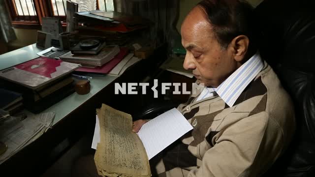 Indian man in European clothes at the table reads the text on the old yellowed paper Indian male,...