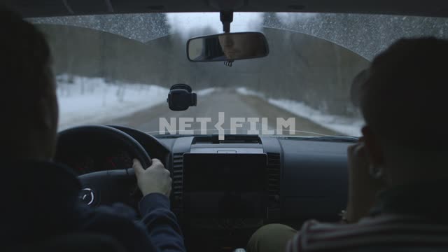 Вид из кабины. Двое мужчин едут по зимней дороге где-то в России. Пассажир играет на губной...
