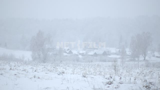 Машина едет по заснеженному полю на фоне деревни. Заснеженная деревня, Россия,  снег, снегопад,...