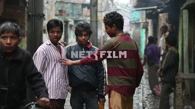 Парни стоят и общаются на одной из небольших улиц в индийских трущобах Парни, общение, трущобы