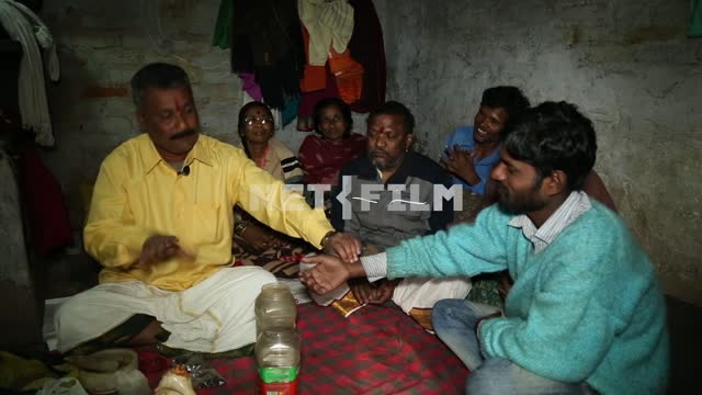 Indian healer in the slums conducts reception of patients. around sitting patients The healer, the...