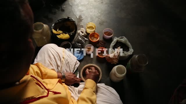 The man in the yellow robe crushes the mortar and drugs, near-capacity with colored powders Drugs,...