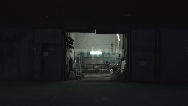 Мужчина работает в гараже Гараж, мужчина за работой, защитный костюм, ночь, темно, свет от лампы