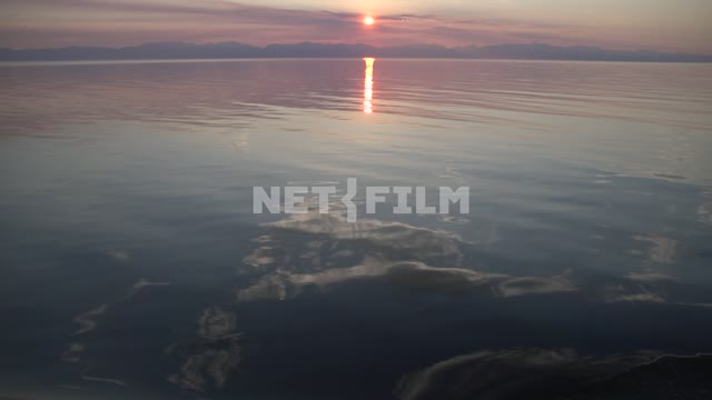 Summer sunset on the lake, the rays of the sun and clouds are reflected in water, mountains in the...