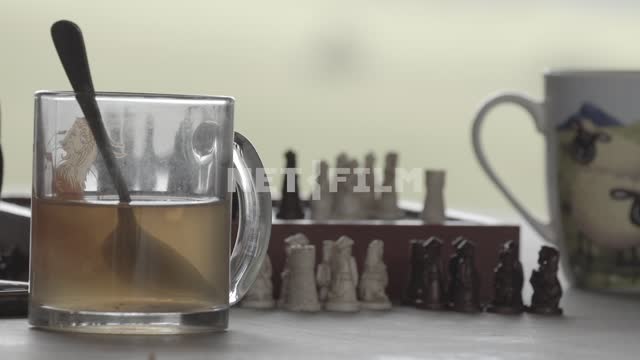 Close-up.
Cups of tea, a chess Board, the pieces.
Hands to assemble chess, and carry the...