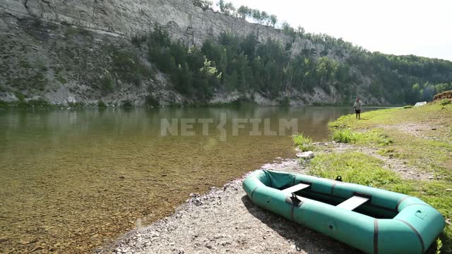 Природа Урала, на берегу реки лежит надувная лодка, вид на противоположный скалистый берег...