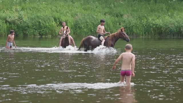 Дети купают лошадей в реке, мимо проплывают туристы на плоту из надувного катамарана Урал,...