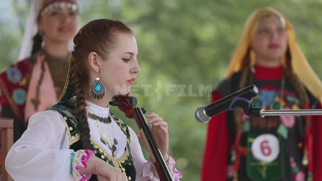 Национальный праздник, на сцене фольклорный ансамбль, девушка играет на кыл-кубызе и поет Урал,...