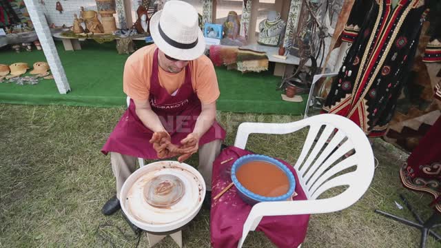 A man kneads wet clay, works on a potter's wheel Ural, Salavatsky district, holiday, fair,...