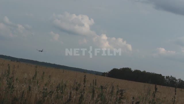 Самолет низко пролетает над полями, съемка с наклоном камеры Урал, небо, облака, кроны деревьев,...