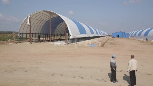 Hangar frames under blue-and-white awnings, workers talking on the construction site Ural,...
