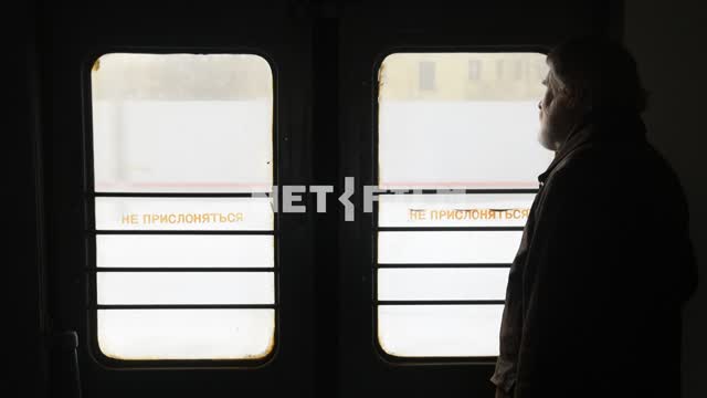 An elderly man in the vestibule of a moving train in winter Door, do NOT LEAN, man, the winter...