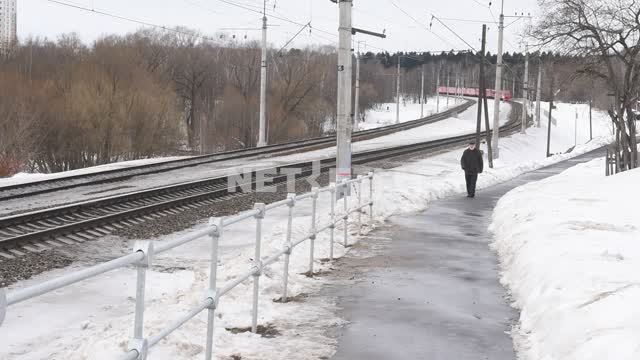 An elderly man walks along the road along the railway track Winter, train, railway, man, snow, road
