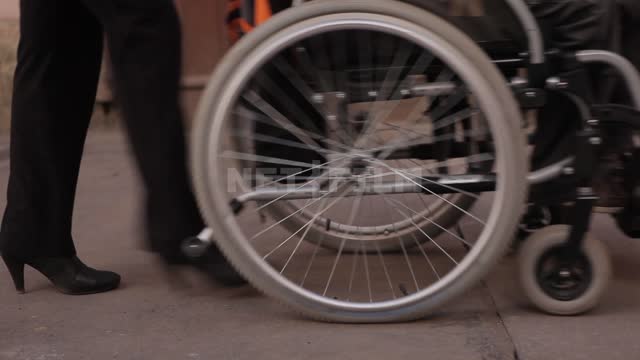 A woman carries a man in a wheelchair along the sidewalk Legs, wheelchair, wheels, sidewalk