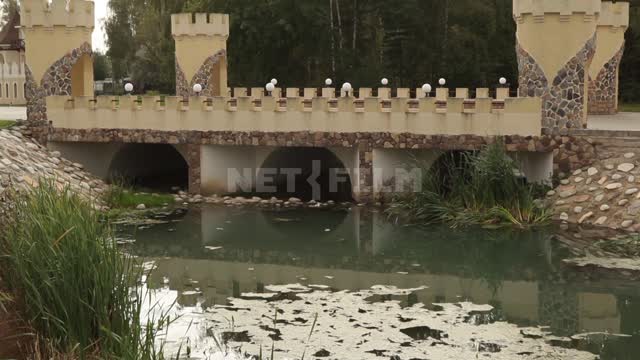 Cottage village, stylized old bridge with turrets Bridge, towers, pond, sedge, mud, trees