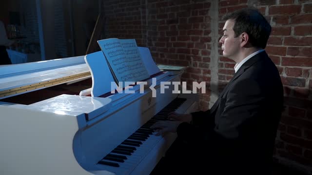 A man plays a white piano Piano, sheet music, people, men, waiters, counter tables, brick wall