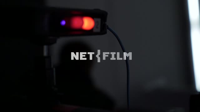 On the movie camera, the indicators are lit, and the silhouette of the operator is visible behind...