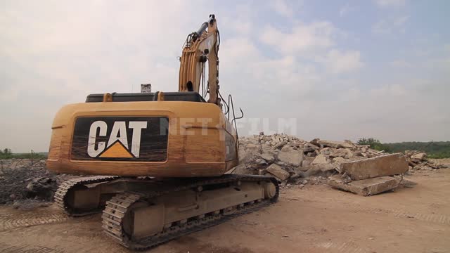 An excavator with a narrow bucket rakes the blockage, puts aside pieces of concrete slabs...