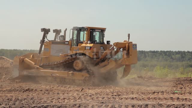 The bulldozer rakes the ground, clears and levels the site Bulldozer, road equipment, earth, clay,...