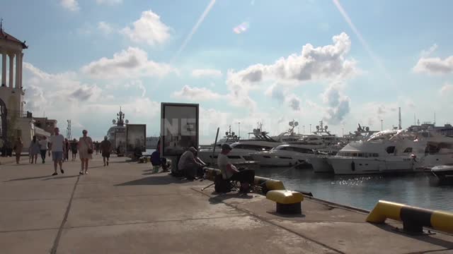 Морской порт, пришвартованные яхты, сидят рыбаки с удочками, гуляют туристы Порт, набережная, яхты,...