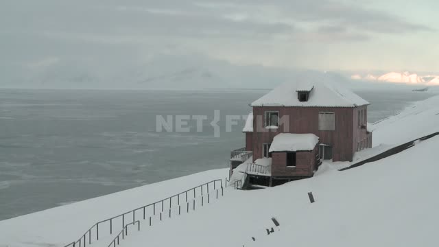 Деревянный дом над берегом моря, Русский север, море, горы, снег, облака, холм, забор.