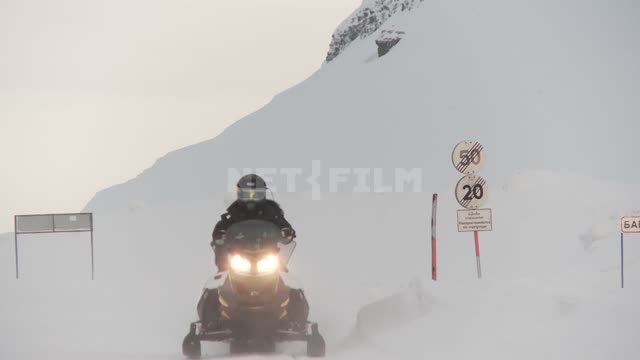 Два мужчины на снегоходах с зажженными фарами едут по дороге. Русский север, зима, снег, автосани,...