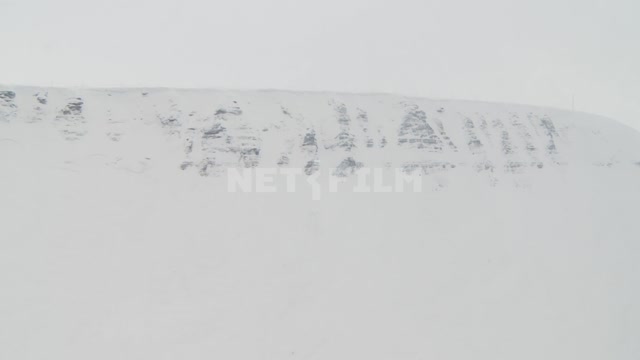 Пролет на вертолете над ледником вдоль заснеженных гор. Русский север, горы, гряда, берег, снег,...