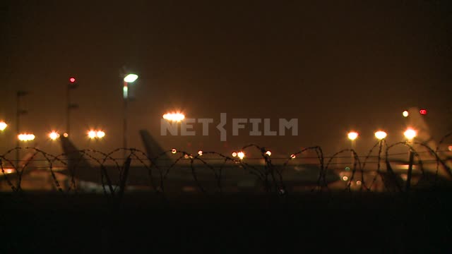 Ночью самолеты стоят на летном поле на фоне огней аэропорта. Аэропорт, транспорт, самолет,...