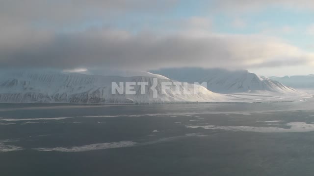 Съемка через иллюминатор вертолета заснеженных гор и моря. Русский север, горы, море, снег, ледник,...