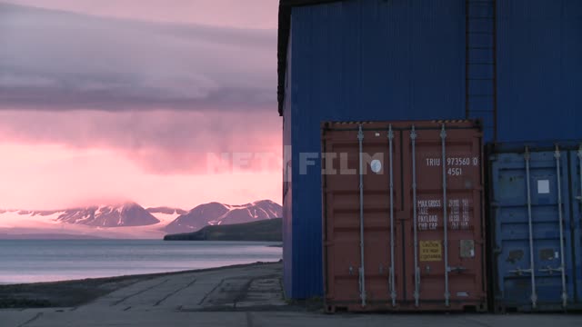 Грузовые контейнеры стоят возле ангара в порту. Русский север, порт, ангар, море, горы, груз.