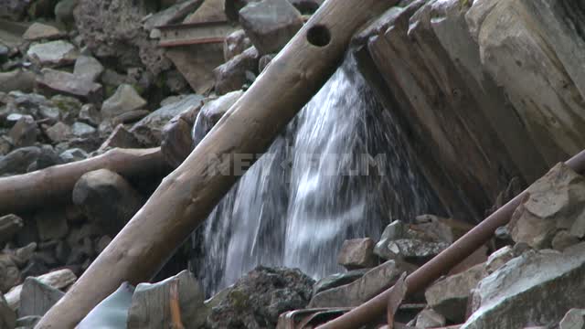 The stream flows over the rocks, boarded-up old wooden building on the hill Russian North, hill,...