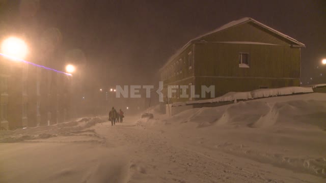 People walk along a snowy street in a snowstorm Russian North,people, winter wear, street lights,...