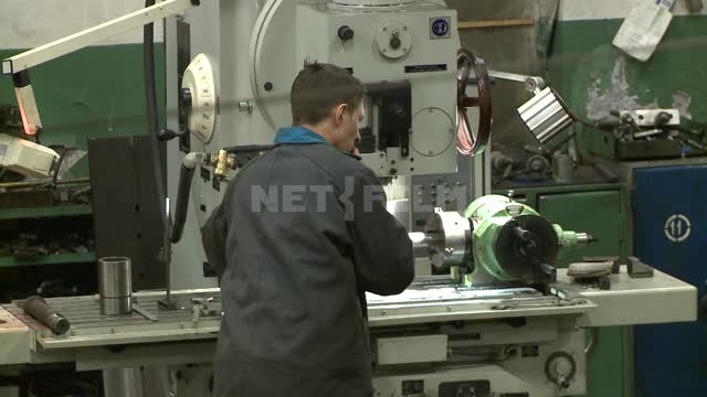 A worker adjusts a milling machine. Russian North, lathe, mill, workbench, detail, drill, frame.