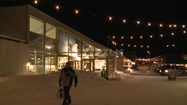 Светятся окна супермаркета Svalbardbutikken, пешеход идет по улице. Русский север, ночь, улица,...