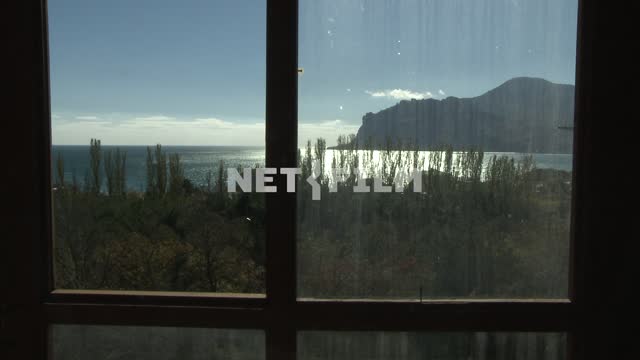 Вид через оконное стекло на горы, море и растительность. Коктебель, горы, море, деревья, день.
